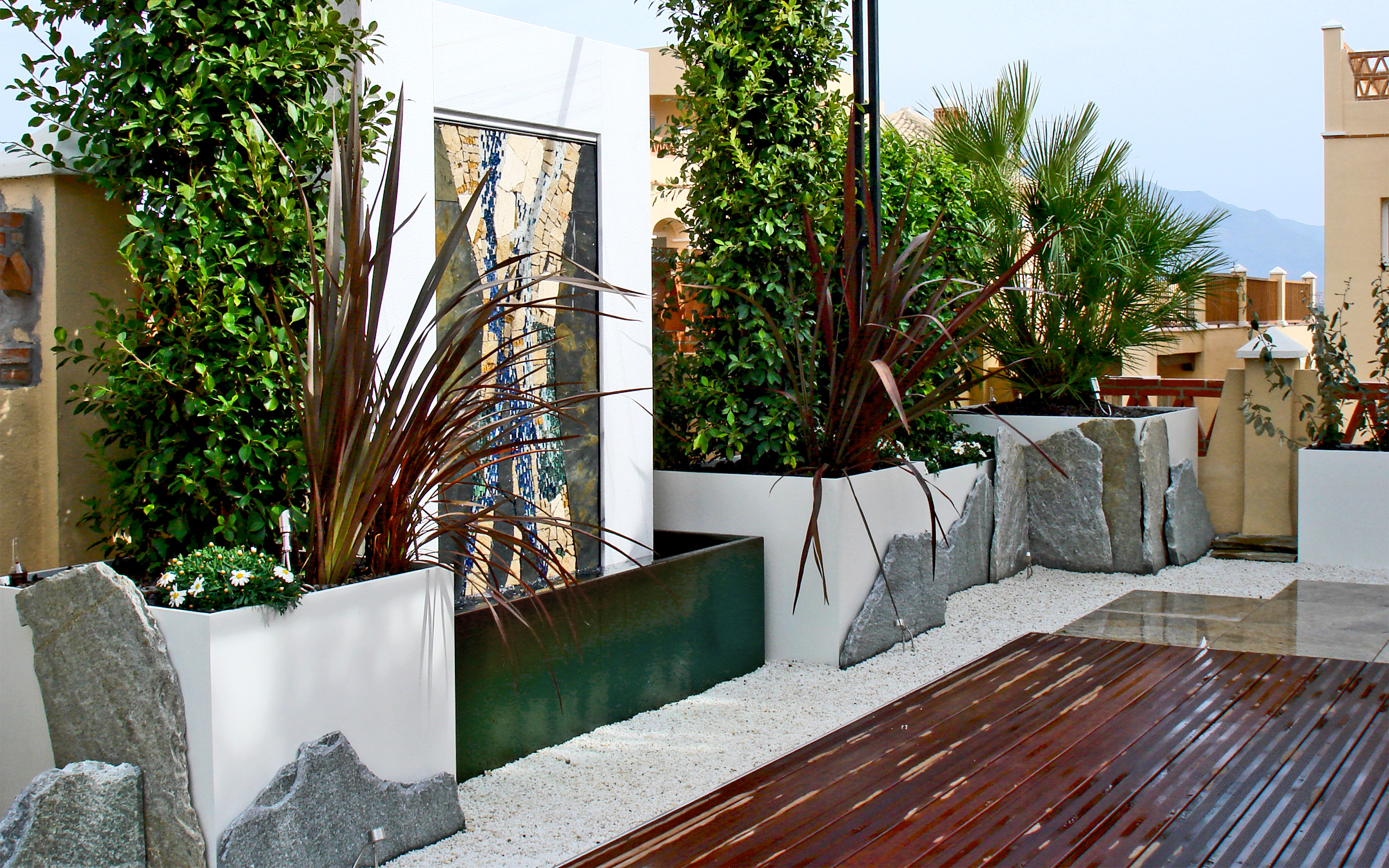 Terraza jardín con la fuenta y pavimentos de madera, granito y cuarzo